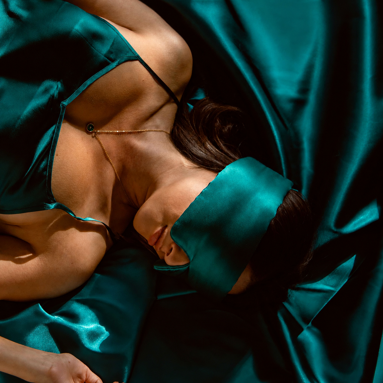 Woman resting in the Green Premium Sleep Mask on silk bedding